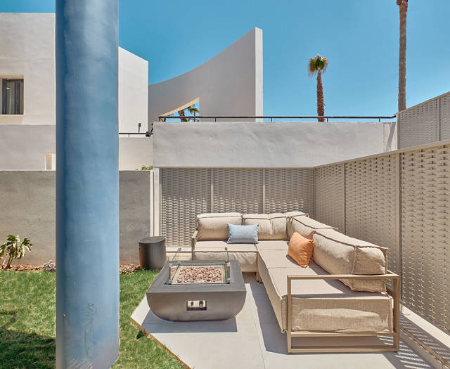 Private garden lounge area with corner sofa, fire pit table, and surrounding privacy walls.