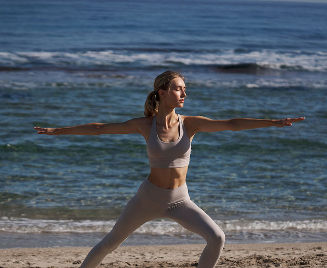 Woman doing yoga pose on a sandy beach with ocean waves in the background.