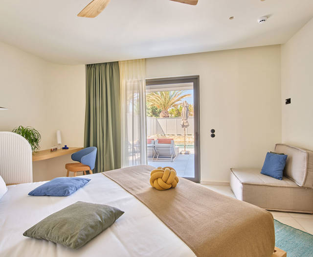 Modern suite with king-size bed, a sofa, a desk and direct access to private pool area.