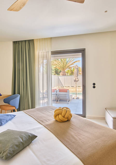Modern suite with king-size bed, a sofa, a desk and direct access to private pool area.
