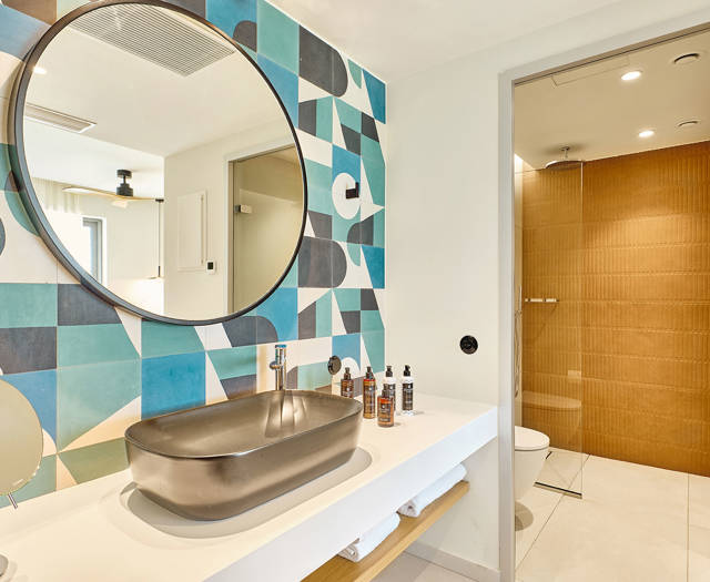 Double room's modern bathroom with vessel sink, large round mirror, and walk-in shower with wooden-style tiles.