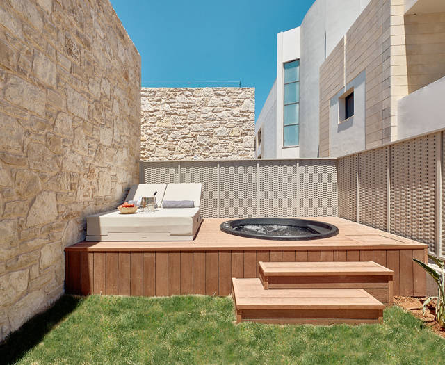 Private garden with wooden deck, hydromassage tub, sun lounger, and stone walls for privacy.