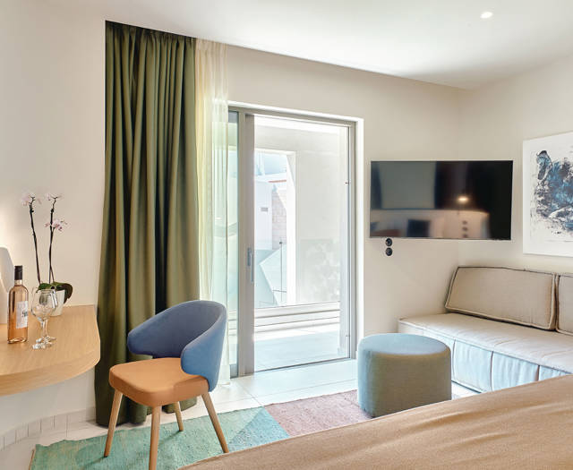 Cozy junior suite corner with a TV, sofa, round table, and sliding door to balcony.
