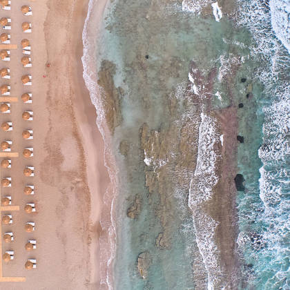 Aerial view of the beach at Kosta Alimia, showing sunbeds on the sand next to the sea and rocky shoreline.