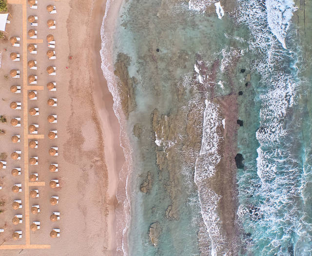 Aerial view of the beach at Kosta Alimia, showing sunbeds on the sand next to the sea and rocky shoreline.