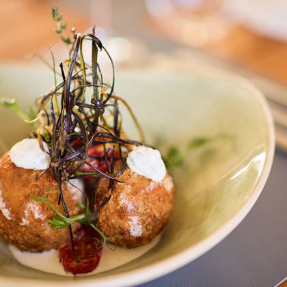 Golden-fried croquettes topped with herbs and cream sauce, artistically plated in a deep ceramic bowl.
