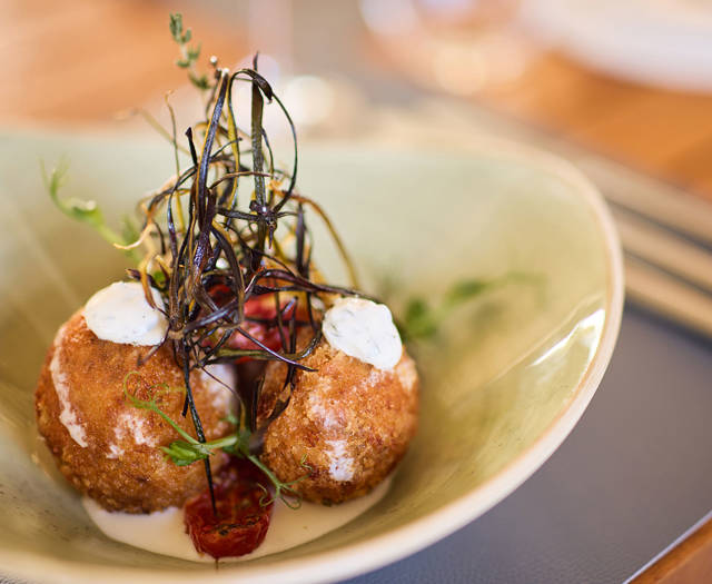 Golden-fried croquettes topped with herbs and cream sauce, artistically plated in a deep ceramic bowl.