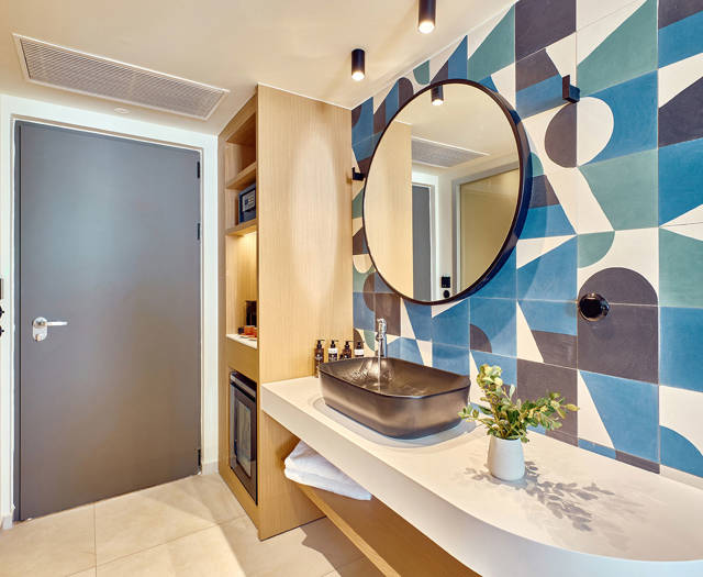 Bathroom entrance with designer sink, geometric tile wall, and built-in shelving with minibar and safe.