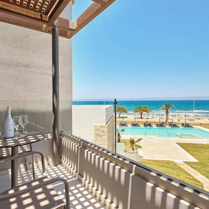 Junior suite's private balcony with two chairs and a table having a side sea view