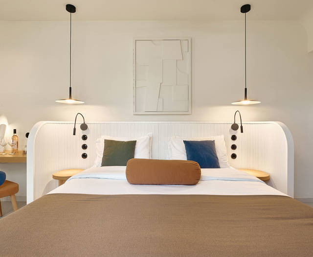 Double bed with neutral bedding, pendant lights, and decorative wall art in a private garden room.
