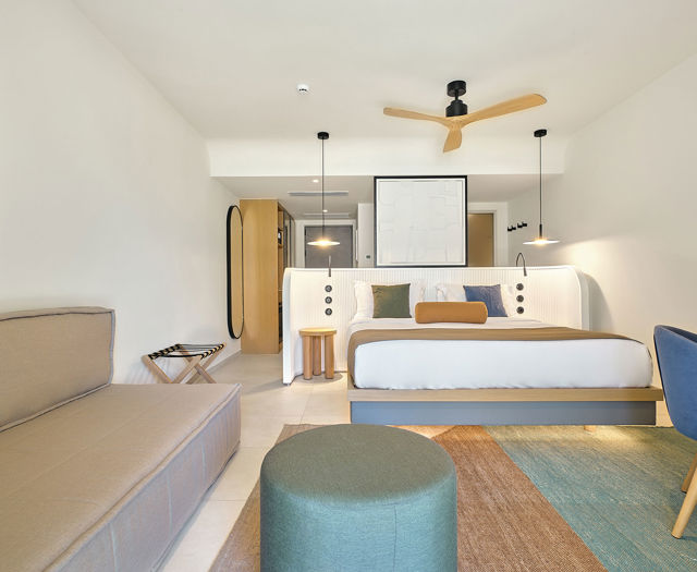 Bright junior suite with double bed, sofa, blue and green chairs, and colorful area rug.