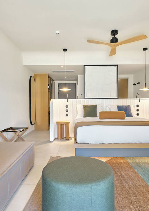 Bright junior suite with double bed, sofa, blue and green chairs, and colorful area rug.