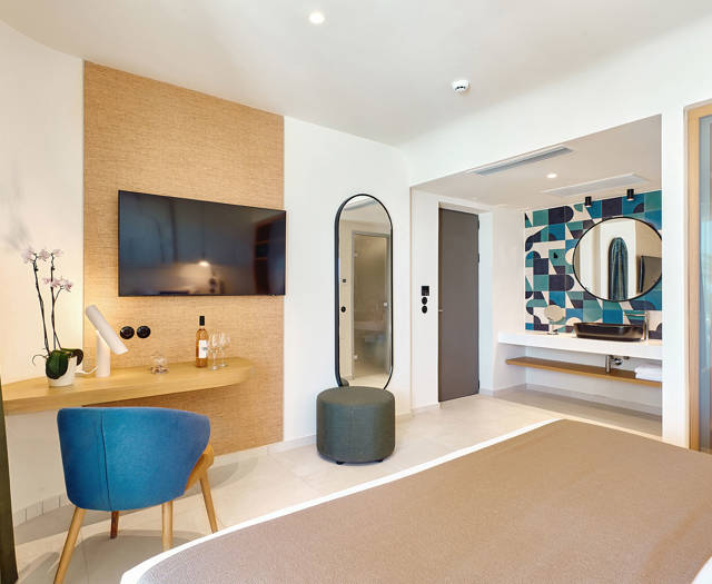 Dooble room with flat-screen TV, vanity desk, and view into the colorful bathroom area.