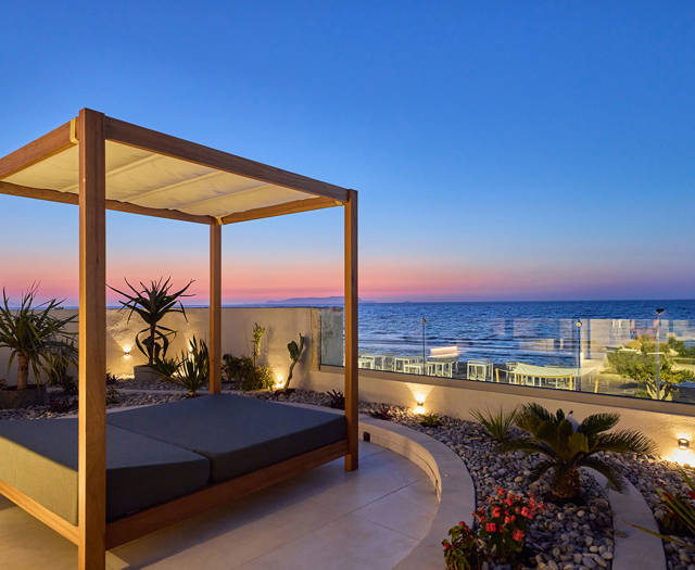 Canopy daybed on a private terrace overlooking the sea at sunset.
