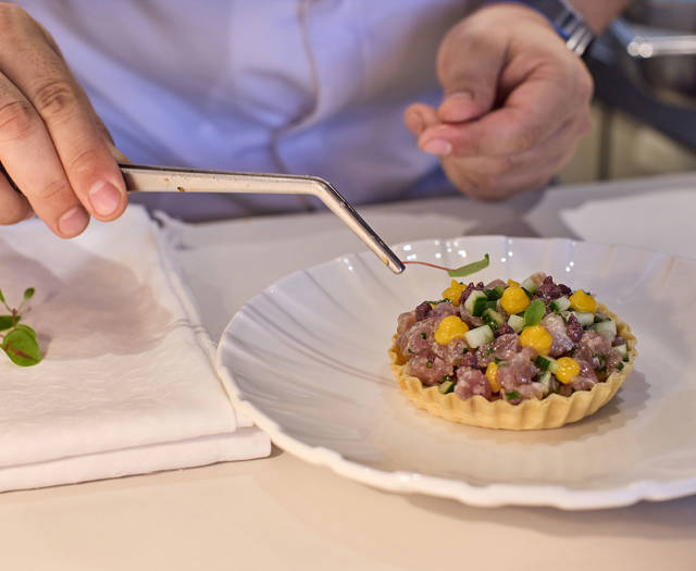 Chef delicately garnishing a tart filled with tuna tartare, mango, and herbs using precision tweezers.