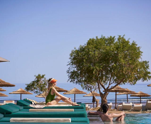Woman relaxing on a sunbed by the sea while man lounges in the pool at Kosta Alimia