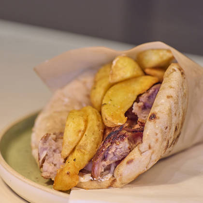 Traditional Greek pita wrap filled with grilled meat, red onions, and golden fried potatoes.