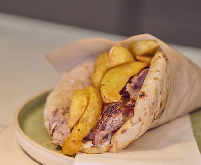 Traditional Greek pita wrap filled with grilled meat, red onions, and golden fried potatoes.