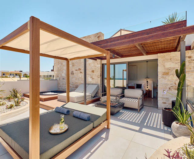 Sunlit terrace with canopy daybed, lounge chairs, and outdoor seating in front of a stone wall facade.
