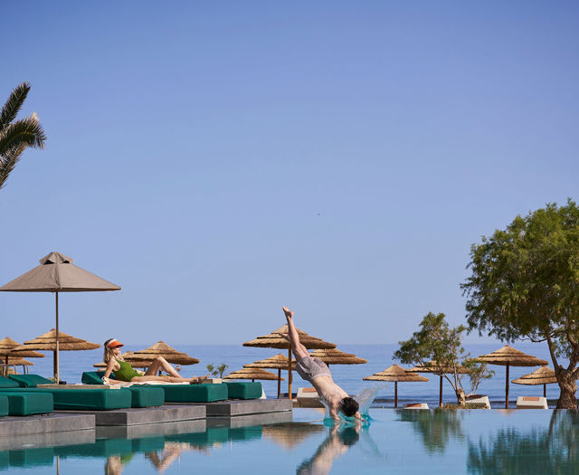 Man diving into pool near sunbeds and palm trees by the sea