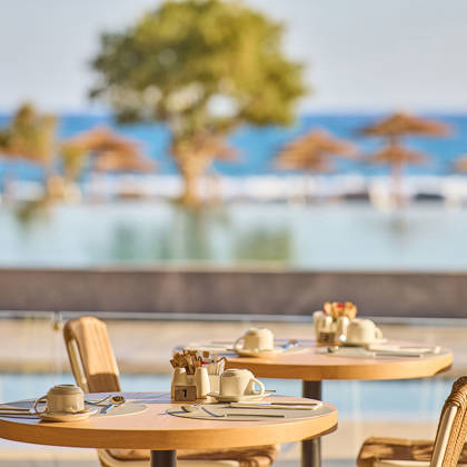 Breakfast tables set by the pool with a sea view in the background.