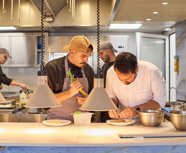 Chefs meticulously plating dishes in a professional open kitchen under warm hanging lights.