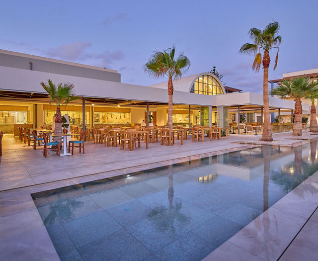 Elegant open-air restaurant at dusk with palm trees, warm lighting, and a reflecting pool in the foreground.