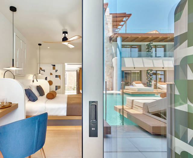 Interior view of a swim-up room with workspace and bed, looking out to the pool through a sliding glass door.