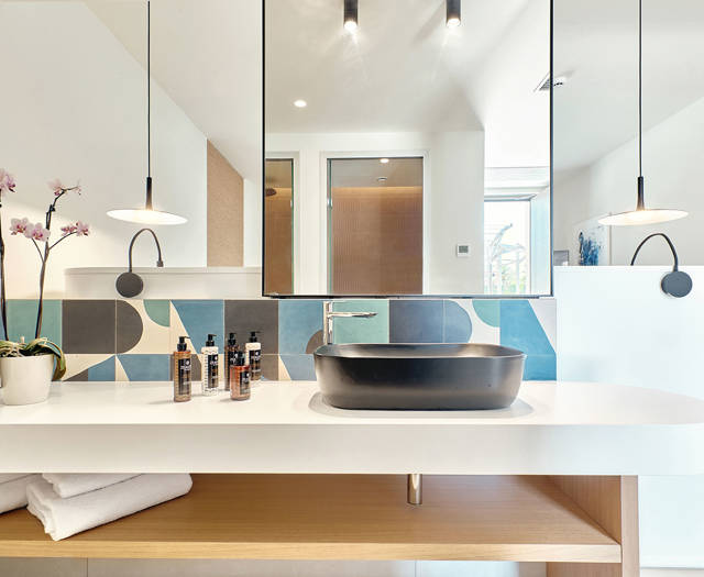 Modern bathroom with geometric tile backsplash, black sink basin, and large mirror above a white countertop.