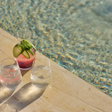 Glasses and a carafe with drinks by the pool edge.