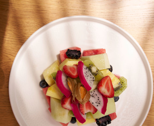 Colorful fruit salad with kiwi, dragon fruit, berries, and melon, served on a white plate.