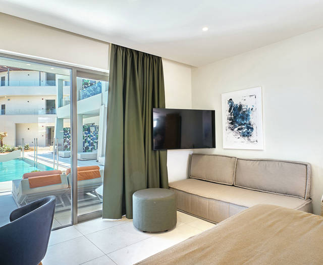 Cozy junior suite corner with a TV, sofa, and sliding door to the pool.