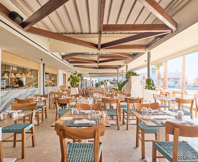 Bright and airy seafood restaurant with open kitchen, wooden beams, and a poolside view
