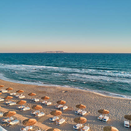 Wide view of the beach with sunbeds under straw umbrellas next to the sea