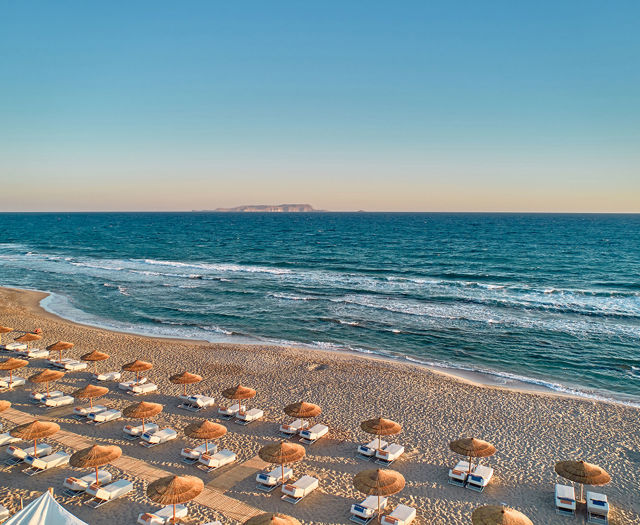 Wide view of the beach with sunbeds under straw umbrellas next to the sea