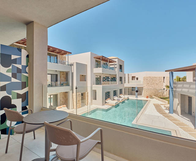 Double room balcony with seating overlooking the pool and modern garden-view hotel buildings
