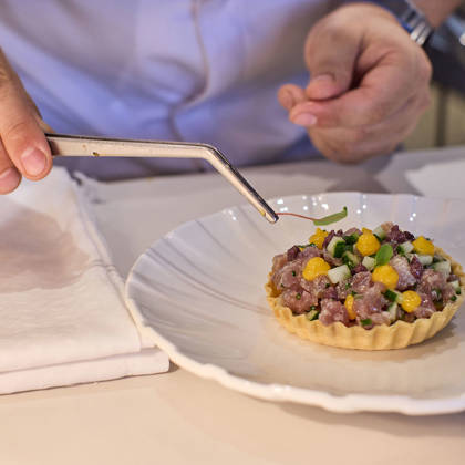Chef delicately garnishing a tart filled with tuna tartare, mango, and herbs using precision tweezers.